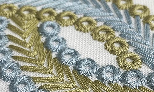 Detail of embroidery stitches in light blue and green on an off-white background.