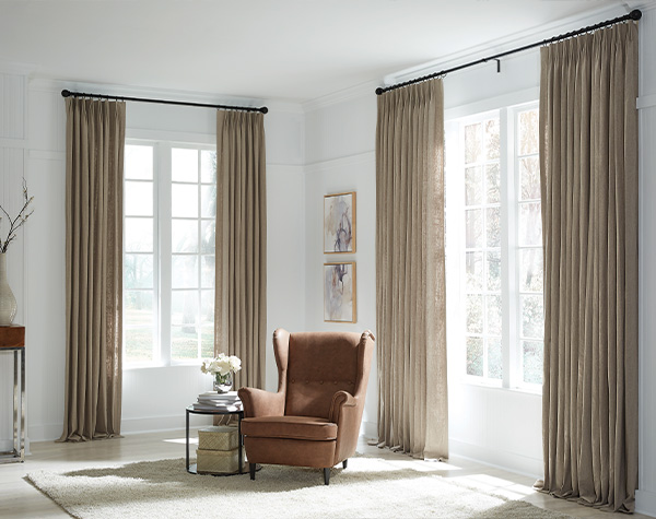 An armchair in a neutral colored room with drapery made from fabric that is one hundred percent recycled polyester to show the beauty of the commitment to sustainability from Carole Fabrics.