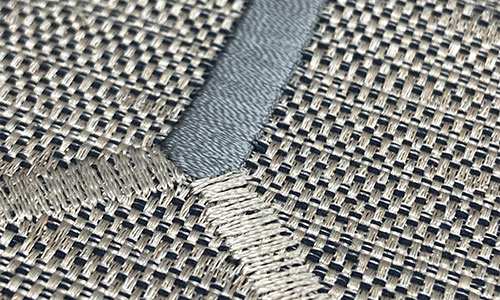 Detail of beige and grey embroidery stitches on a two-toned neutral background.