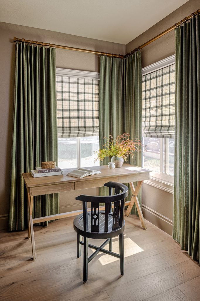 A casual corner office in green and natural colors, featuring two windows with Flat Roman Shades in a large scale plaid pattern and green draperies with verical stripes.