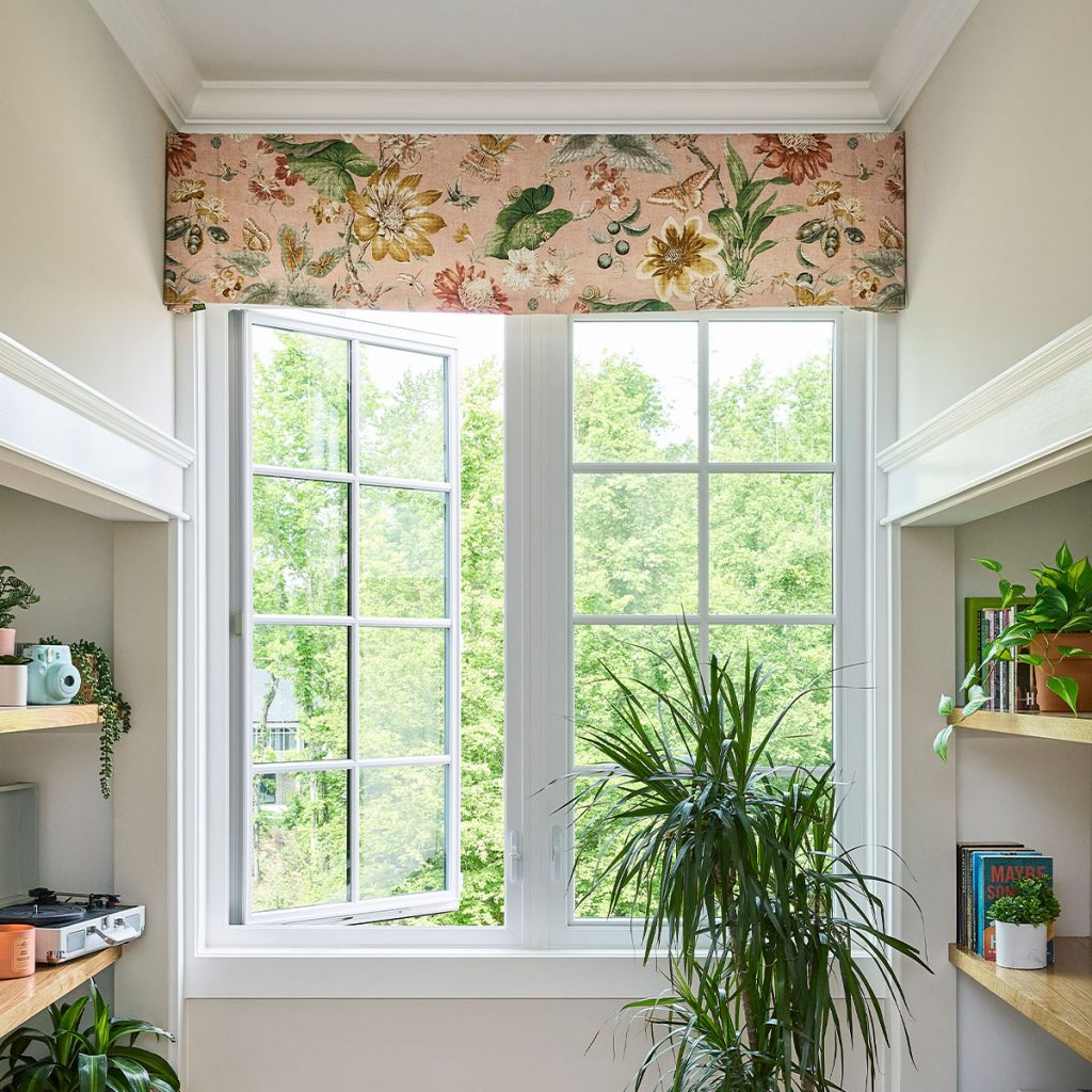 A large window at the end of a shelved hallway with a Madison Board Mounted Valance in a large scale floral fabric with a pink background.