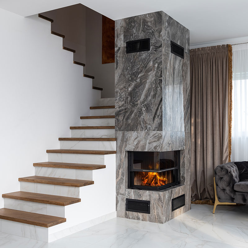 A lit fireplace in a room between an open staircase and fringed draperies.
