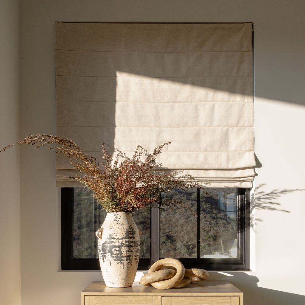 Dramatically lit Reverse Fold Roman Shade in a solid neutral fabric.