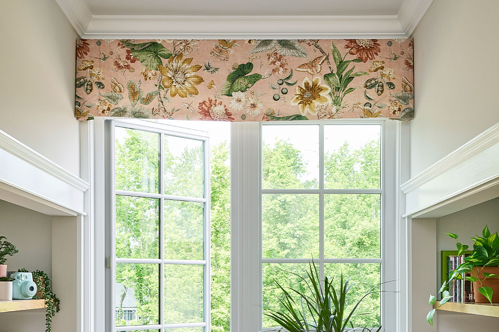 A pink floral board mounted valance over an open window with shelves on either side.