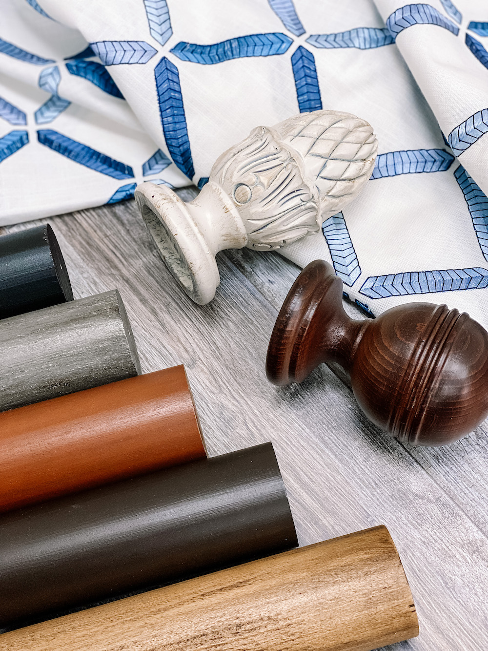 Close up of Forest Magnolia wood drapery hardware and two styles of finials next to draped white and blue patterned fabric from Carole Fabrics.