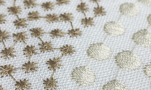 Detail of star and dot shaped embroider in light neutral colors on a white background.