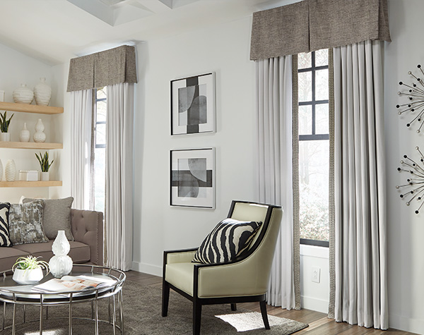 A living room in light neutral featuring drapery, valances and pillows from Carole Fabrics.
