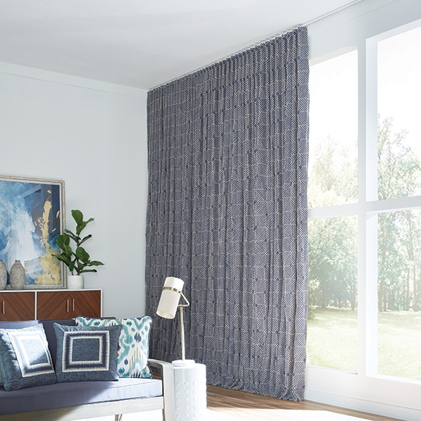 Dark blue ripplefold drapery on a wall of windows with bright sunlight streaming into the living room.